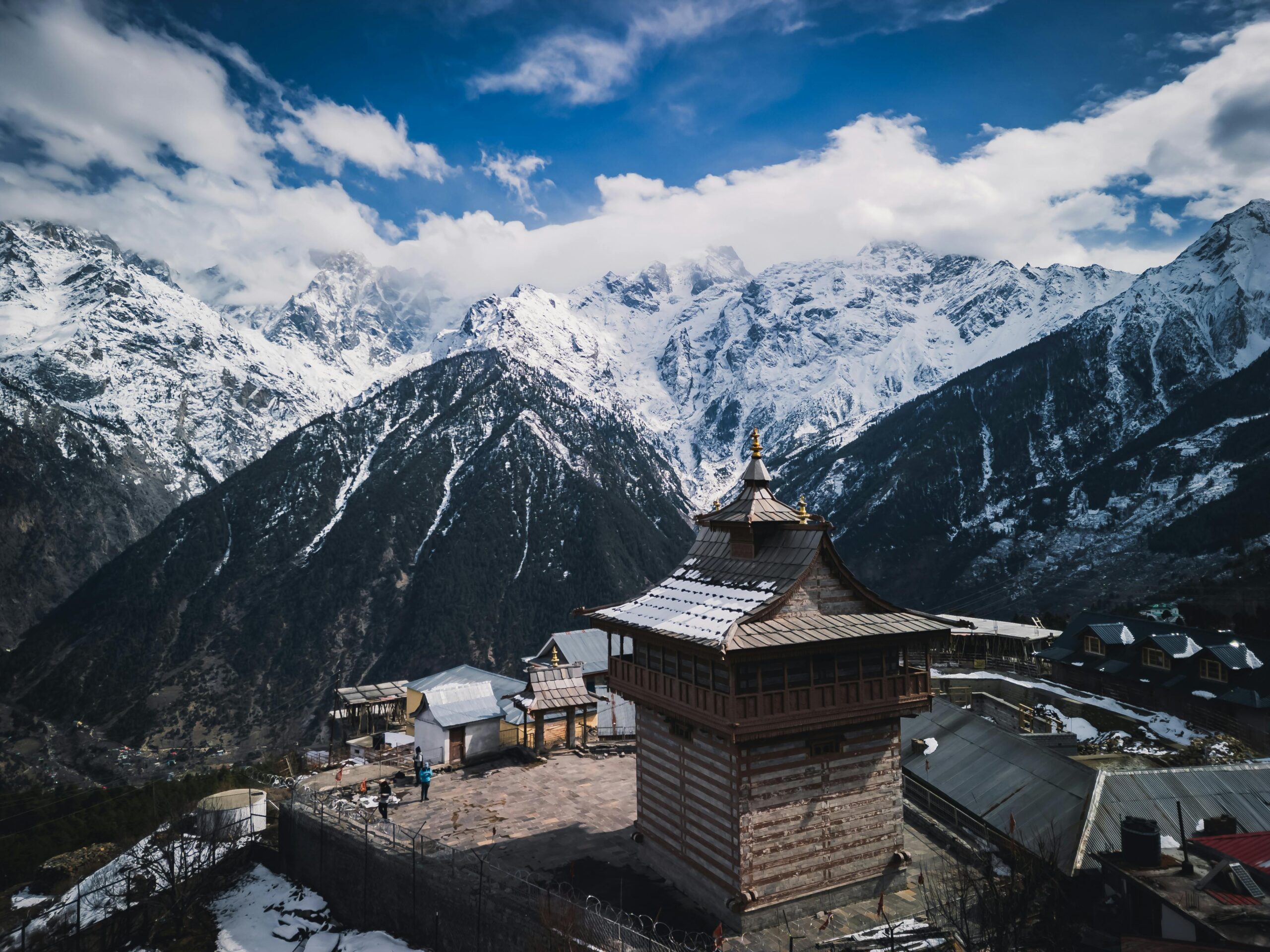 Stunning view of Kinnaur Kailash temple and snow-covered Himalayan mountains under a vibrant sky.