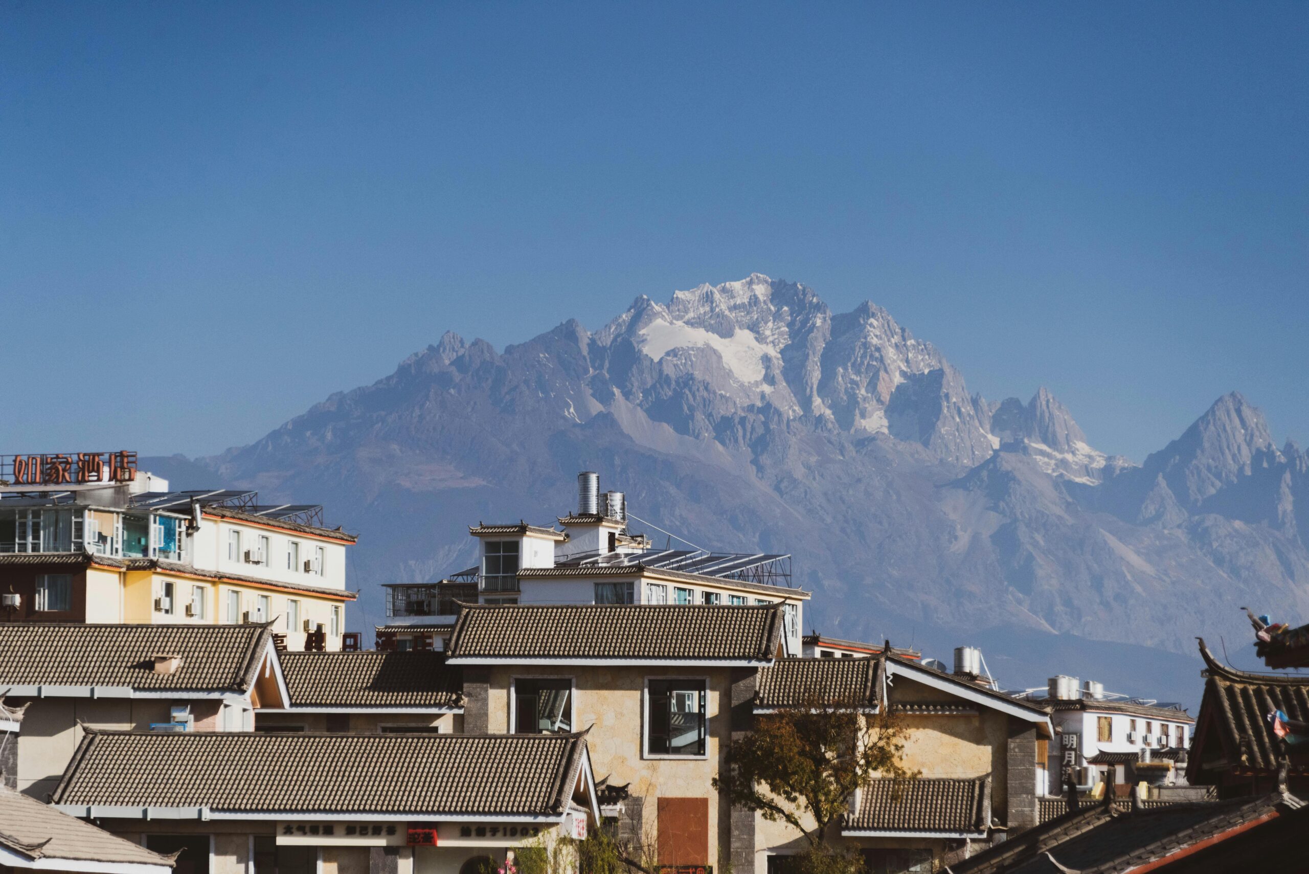 Charming town with traditional roofs against majestic snow-capped mountains on a clear, sunny day.